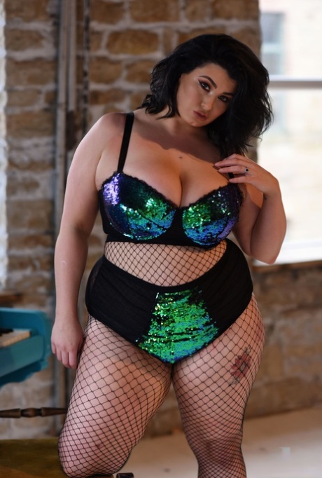 BBW babe Kiki poses in fishnets & strips to cradle her colossal breasts