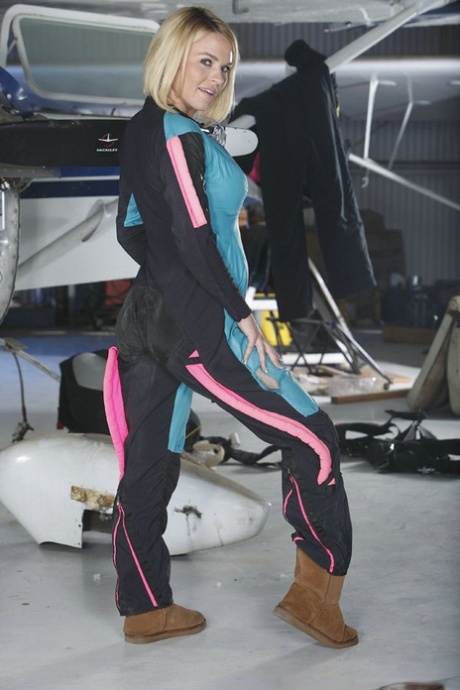 Blonde chick unzips her jumpsuit for artistic poses inside an aircraft hangar