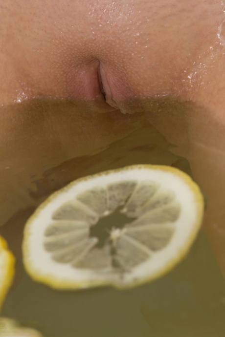 Cute blonde young adult sinks her bald twat into a tub filled with lemon slices