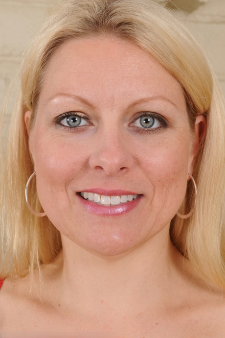 Middle-aged blonde woman Zoey Tyler poses in stockings by the fireplace